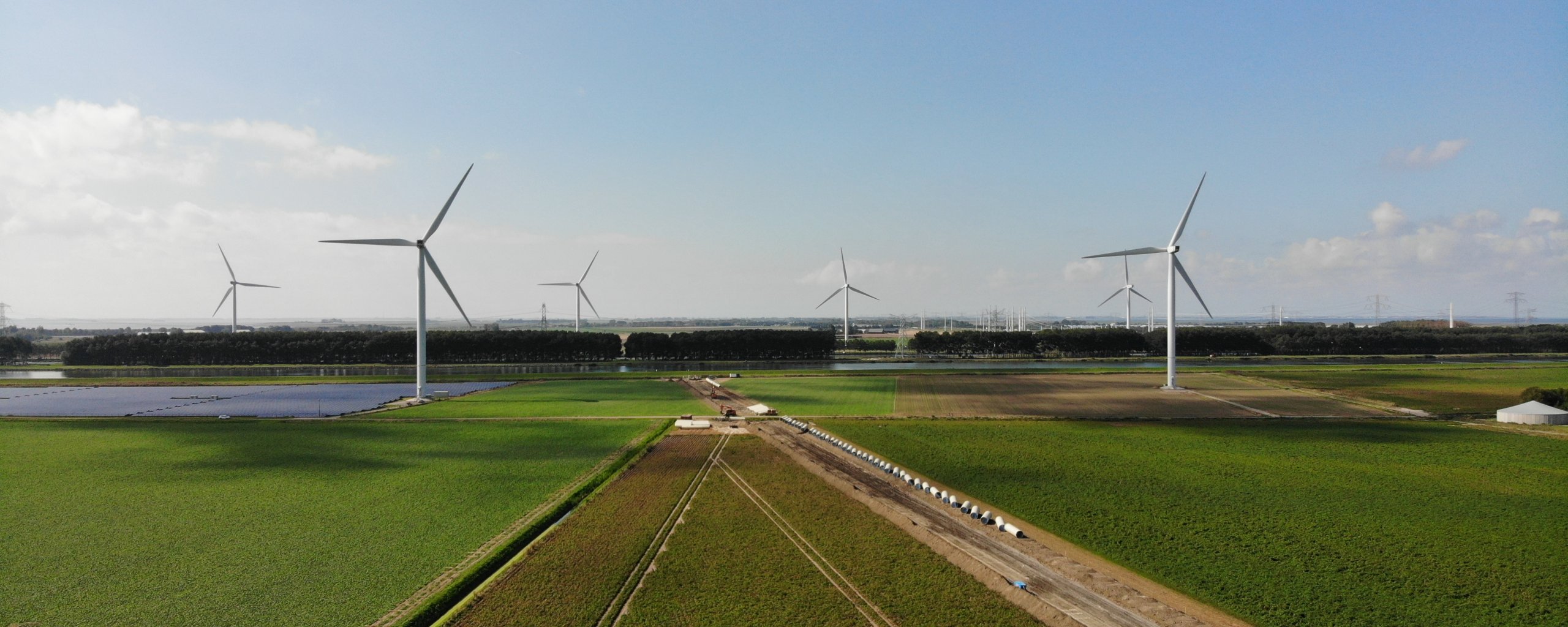 Windmolens, groene weilanden, witte betonnen buizen op een rij.