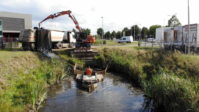 Medewerker in boot in het water aan het baggeren